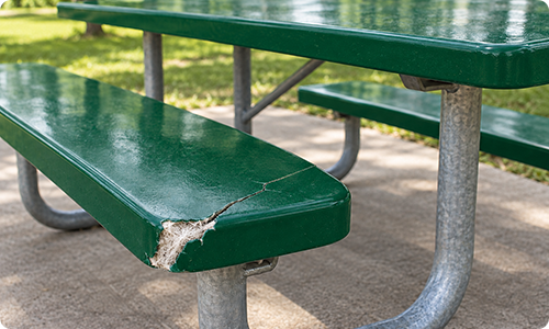 Green fiberglass picnic table bench with a chipped edge, exposed fibers, and a crack near the support.